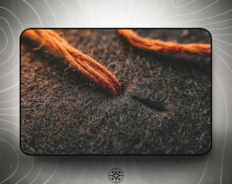 Puede incluir: Una vista de cerca de un material oscuro, texturizado y similar al fieltro que presenta dos hilos fibrosos de color naranja que emergen de pequeñas aberturas precisas. La superficie tiene un aspecto denso y difuso con fibras visibles y hilos deshilachados.