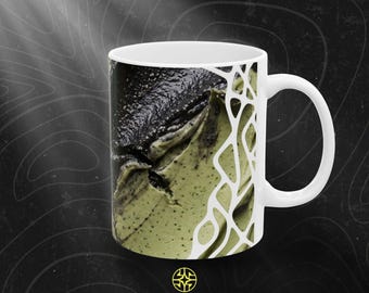 Puede incluir: Una taza de cerámica blanca con un estampado gráfico de una sustancia texturizada de color negro y verde claro. El diseño incluye un patrón de red orgánica blanca en el lado derecho. El texto ASSEMBLE WONDER aparece en la parte inferior.