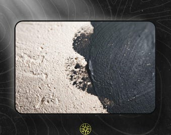 Puede incluir: Una superficie texturizada con un diseño de alto contraste que presenta un área rugosa, porosa y de color blanco hueso que transiciona hacia una sección pintada en negro sólido y liso. El borde entre ambos colores muestra detalles salpicados.