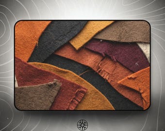 Puede incluir: Una colección de retazos de tela de fieltro superpuestos en varios tonos tierra, incluyendo naranja quemado, negro carbón, amarillo mostaza, burdeos intenso y marrón. Las piezas presentan bordes irregulares y una textura fibrosa y suave.