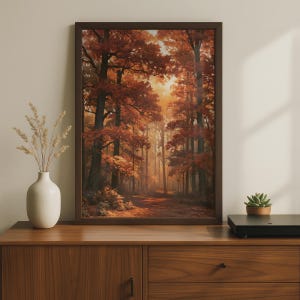 May include: A rectangular framed wall art print depicting a forest scene with tall trees featuring dense orange and red autumn foliage. The artwork is displayed in a dark brown frame, capturing a sunlit path winding through the woods.