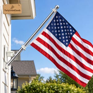 May include: A United States flag attached to a silver metal pole mounted on a white wall. The flag features thirteen horizontal red and white stripes and a blue canton with fifty white stars. A wooden sign with the text PartyUnitedGoods is visible.