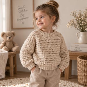 May include: A beige long-sleeved knit jumper with a textured pattern, a round neckline, and ribbed cuffs and hem, paired with light tan corduroy trousers. The jumper features a thick, chunky knit construction with a consistent weave throughout.