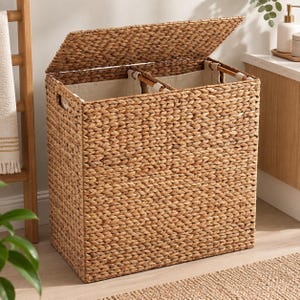 May include: A rectangular laundry hamper crafted from woven brown seagrass with a hinged lid. The interior features two separate compartments lined with off-white fabric, each supported by a wooden frame and integrated handles on the sides.
