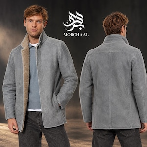Può includere: Una giacca in camoscio grigio con fodera in montone color cuoio, collo alto e chiusura con bottoni. La giacca è mostrata di fronte e di schiena, con il logo e la scritta Morchaal sopra. La giacca è indossata sopra una camicia azzurra.