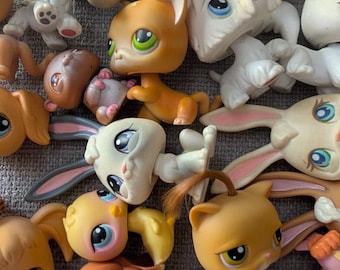 May include: A collection of various plastic animal figurines featuring large eyes and stylized features. The group includes cats, dogs, rabbits, and other creatures in shades of white, brown, orange, and yellow, all arranged in a dense cluster.
