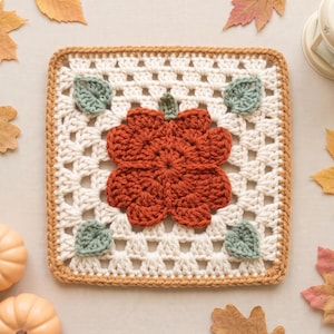 May include: A square crochet granny square featuring a central dark orange pumpkin motif with a small green stem. The pumpkin is surrounded by four small sage green leaves on a white open-work background, all bordered by a solid tan yarn edge.