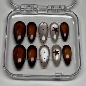 Puede incluir: Un juego de diez uñas postizas en forma de almendra dispuestas en un estuche de plástico transparente. Las uñas tienen un acabado brillante con una mezcla de degradado marrón oscuro, beige claro con puntos marrones y estrellas marrones.
