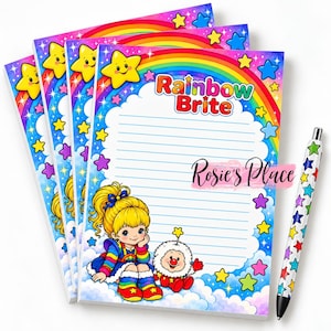 May include: A stack of four Rainbow Brite stationery sheets featuring a colorful rainbow, yellow stars, and a cartoon character with blonde hair and a white fluffy creature. The text Rainbow Brite and Rosie's Place is printed on the lined paper. A matching pen with a star pattern is included.