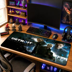 以下が含まれることがあります： ビデオゲーム「Detroit: Become Human」のロゴとキャラクターアートが描かれた長方形のデスクマット。マットには、3人の人物と青い光のアクセントが特徴的な暗い映画のようなシーンが描かれており、木製のデスクの上に配置されています。