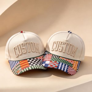 以下が含まれることがあります： フロントパネルに盛り上がったブロック体で「CUSTOM」という文字が刺繍された、オフホワイトの野球帽2点。つばの部分には、ストライプ、チェック柄、小さな花柄が組み合わさった、鮮やかな色合いのパッチワーク模様が施されています。