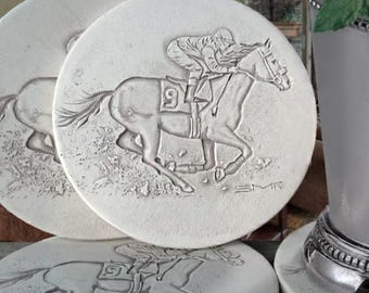 May include: Three round white stone coasters featuring an embossed design of a jockey riding a racehorse with the number nine on its side. A silver-toned metal cup with a beaded base sits on one of the coasters, containing ice and mint leaves.