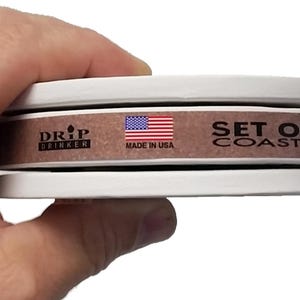 May include: A set of four brown cork coasters with a white border. The coasters are stacked on top of each other. The top coaster has a label that says "Drip Drinker" with a small drop of water icon, a small American flag, and the text "Made in USA". The bottom coaster has a label that says "Set of 4 Coasters".