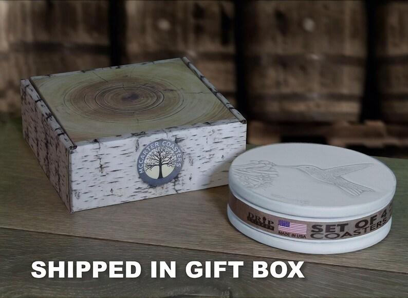 May include: A set of four white ceramic coasters with a hummingbird design. The coasters are packaged in a white gift box with a birch bark pattern and the text "McCarter Coasters" printed on the box.