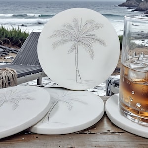 May include: Set of four white ceramic coasters with a black palm tree design. The coasters are round and have a smooth surface.