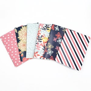 May include: Set of six small notebooks with different patterned covers. The covers feature a variety of designs, including polka dots, floral patterns, stripes, and abstract designs. The notebooks are all black and pink.