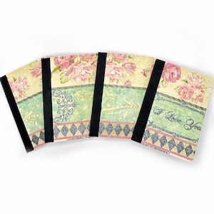 May include: Set of four small notebooks with floral designs and black elastic closures. The covers feature a vintage floral pattern with pink roses, green leaves, and a silver glitter accent. The notebooks have a black and white diamond pattern at the bottom and the words "I Love You" are written on one of the notebooks.