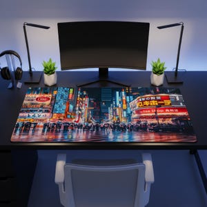 May include: A rectangular desk mat featuring a vibrant night scene of a busy Japanese city street with illuminated neon signs, including text reading Don Quijote and Tax Free Shop, set on a black desk with a computer monitor and two lamps.