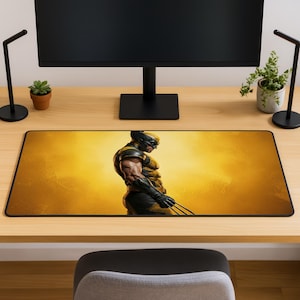 Puede incluir: Una alfombrilla de escritorio rectangular con una ilustración gráfica de un personaje con traje amarillo y negro, máscara y garras metálicas que sobresalen de las manos, sobre un fondo dorado brillante y luminoso.