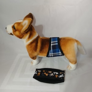 May include: A brown and white stuffed dog wearing a blue and white plaid dog diaper. A black dog diaper with a multi-colored dog print is also shown in the image.