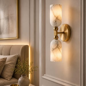 May include: A wall sconce featuring two vertically stacked, fluted white marble glass shades with grey veining. The shades are connected by a central brass-toned metal rod and mounted to the wall with a circular brass-toned metal backplate.