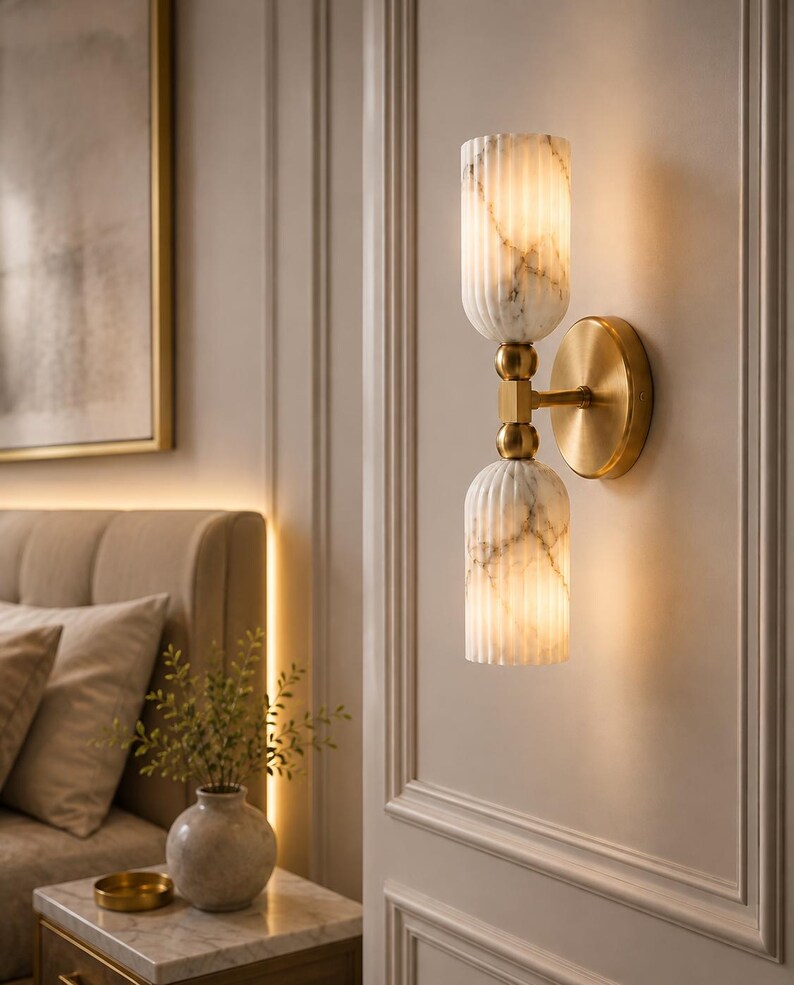 May include: A wall sconce featuring two vertically stacked, fluted white marble glass shades with grey veining. The shades are connected by a central brass-toned metal rod and mounted to the wall with a circular brass-toned metal backplate.