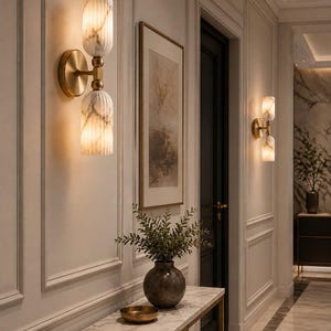 May include: A wall sconce featuring two vertically stacked, fluted, white marble-patterned glass cylinders connected by a brass-toned metal fixture. The light fixture emits a warm glow from both the top and bottom glass shades mounted on a wall.