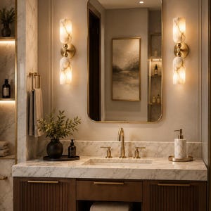 May include: A bathroom vanity featuring a white marble countertop with a gold faucet and handles, a rectangular mirror with a gold frame, and two vertical wall sconces with ribbed glass shades. The dark wood cabinet has fluted doors.