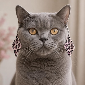 Könnte beinhalten: Ein Paar rautenförmige Perlenohrringe mit einem Leopardenmuster in Rosa, Schwarz und Weiß. Die Ohrringe bestehen aus kleinen, gleichmäßigen Perlen, die in einem geometrischen Muster angeordnet sind und an silberfarbenen Metallhaken hängen.