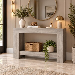 May include: A rectangular console table with a light gray wood grain finish. The table features a flat top surface and a lower shelf. The top holds a white vase with greenery, a decorative wooden knot, books, and a gold lamp. A woven basket sits below.