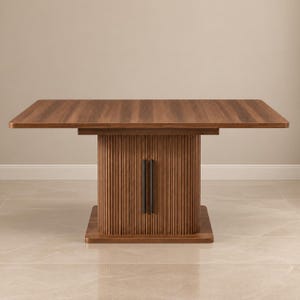May include: A rectangular dining table with a smooth, medium-brown wood grain top. The central pedestal base features a vertical fluted design in a matching wood finish, accented by two slim, vertical black metal handles on the front panel.