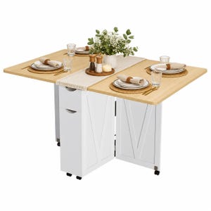 Pode incluir: Uma mesa de jantar dobr&aacute;vel em madeira clara com base branca, apresentando duas gavetas de armazenamento e pain&eacute;is em forma de V. A mesa est&aacute; posta com quatro lugares, incluindo pratos, guardanapos, copos e um arranjo floral central.