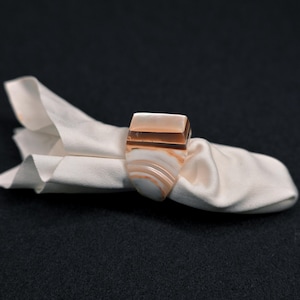 May include: A ring carved from banded agate featuring a rectangular top and a smooth, polished surface. The stone displays natural layers of translucent white, cream, and warm brown tones, creating a distinct striped pattern throughout the band.