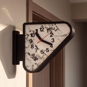 May include: A triangular wall-mounted clock with a black frame and a white face featuring a black marble pattern. The clock has black hour and minute hands, a thin red second hand, and black Arabic numerals from one to twelve.