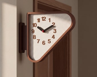 May include: A wall-mounted clock with a triangular frame in a dark brown finish. The clock face features a white grid pattern background with dark brown numerals from 1 to 12. It has two dark hands and a small red center cap for the movement.