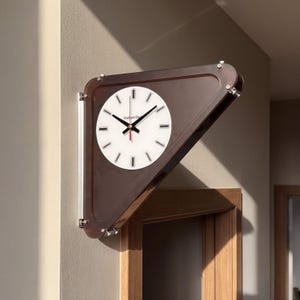 Op de afbeelding: Een driehoekige wandklok met een donkerbruin doorschijnend frame en een witte ronde wijzerplaat. De klok heeft zwarte uur- en minuutwijzers, een rode secondewijzer en zwarte rechthoekige uurmarkeringen. De tekst Gradient Clock staat op de wijzerplaat gedrukt.