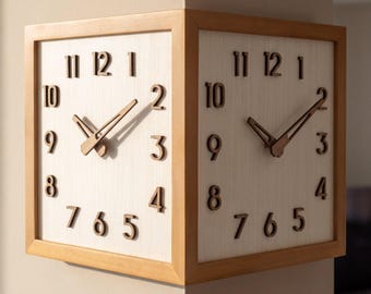 May include: A double-sided corner wall clock featuring two square faces with light wood frames and white textured backgrounds. Each face displays dark brown raised numerals from 1 to 12 and matching dark brown hour and minute hands.