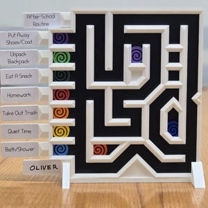 Puede incluir: Un laberinto de madera blanco y negro con las palabras "After School Routine" y "OLIVER" impresas. El laberinto tiene marcadores en espiral coloridos y etiquetas para tareas como "Homework" y "Eat A Snack".