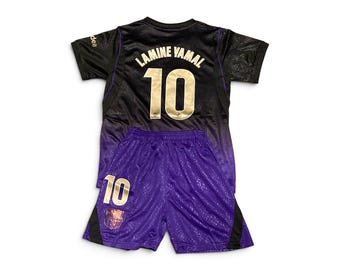 May include: A black and purple sports jersey and shorts set featuring the name LAMINE YAMAL and the number 10 in gold lettering on the back of the jersey. The purple shorts include the number 10 and a team crest on the lower right leg.