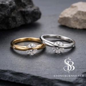 May include: Two rings, one in gold and one in silver, each featuring a central round brilliant-cut stone held by a tension setting. The bands are smooth and polished, with small accent stones embedded along the sides of the metal shanks.