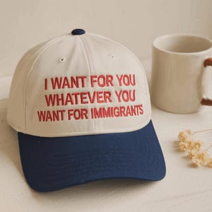 Könnte beinhalten: Eine cremefarbene Baseballkappe mit dunkelblauem Schirm und einem dunkelblauen Knopf an der Oberseite. Auf der Vorderseite der Kappe befindet sich ein gestickter roter Text: I WANT FOR YOU WHATEVER YOU WANT FOR IMMIGRANTS. Die Kappe hat eine feste Form.