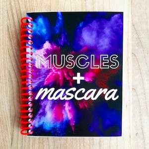 May include: A black spiral bound notebook with a colorful abstract design. The text "MUSCLES + mascara" is printed in white on the front cover.