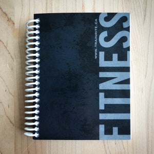 May include: Black and white fitness journal with a spiral binding. The cover has a distressed texture and the word "FITNESS" in large, gray letters. The website "www.trainrite.ca" is printed in white at the bottom right corner.