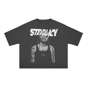 Może przedstawiać: Ciemnoszary t-shirt z krótkim rękawem z dużym białym nadrukiem graficznym z napisem STEVE LACY nad czarno-białym portretem fotograficznym osoby w okularach przeciwsłonecznych i podkoszulku, z widocznymi tatuażami na obu ramionach.