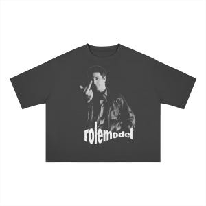 Op de afbeelding: Een antracietgrijs T-shirt met korte mouwen en een zwart-wit fotoprint van een persoon in een jas die een middelvinger opsteekt. Onder de afbeelding staat het woord "rolemodel" gedrukt in witte, vetgedrukte kleine letters.
