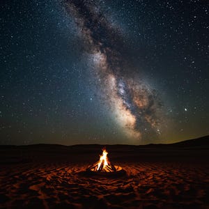 Puede incluir: Una fogata de color naranja y amarillo brillante arde en un pozo de fuego circular de metal situado en un paisaje de arena oscura y ondulada. Sobre el fuego, el vasto cielo nocturno está lleno de estrellas y la galaxia de la Vía Láctea.