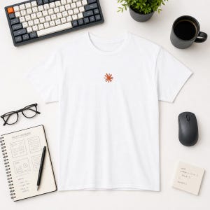 Peut inclure: Un t-shirt blanc à manches courtes orné d'un petit motif de soleil stylisé de couleur rouille centré sur la poitrine. Ce vêtement présente une encolure ronde classique, des manches courtes et une coupe droite simple et épurée.