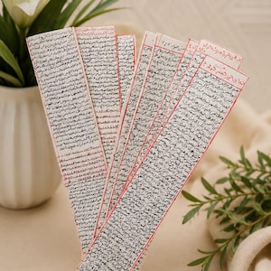 Könnte beinhalten: Drei lange, rechteckige Lesezeichen aus Papier mit dichtem, handgeschriebenem arabischem Text in schwarzer Tinte. Jedes Lesezeichen hat einen dünnen, handgezeichneten roten Rand. Das Papier ist cremefarben und der Text bedeckt die gesamte Oberfläche.