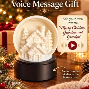 Op de afbeelding: Een witte keramische sneeuwbol met een huis en dennenbomen erin, op een zwarte cilindrische voet. De tekst luidt: Personalized Voice Message Gift, Add your own message: Merry Christmas Grandma and Grandpa, en Audio recorder hidden in the bottom base.