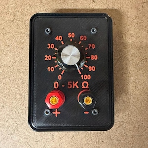Puede incluir: Un módulo de potenciómetro electrónico rectangular negro con una perilla central plateada y un dial marcado de 0 a 100. La placa frontal muestra el texto 0 - 5K Ω en naranja, con un terminal positivo rojo y un terminal negativo negro debajo.